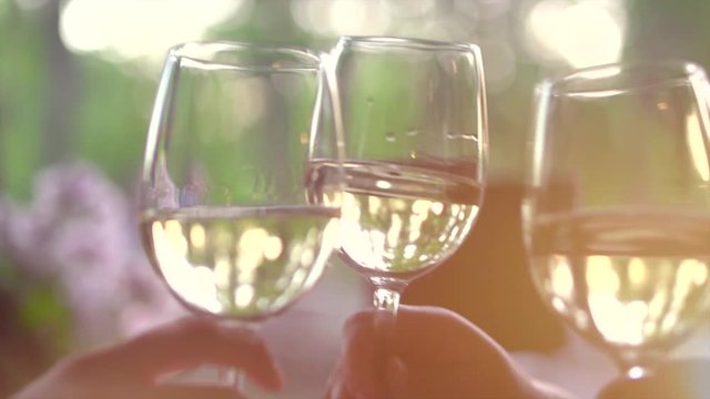 Group of people toasting and drinking white wine on the restaurant terrace over sunset. Glasses with wine over nature background. Slow motion. 3840X2160 4K UHD video footage