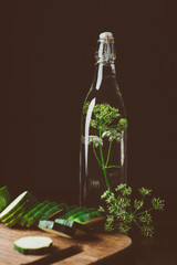 glass bottle with water and dill, cut zucchini on wooden board