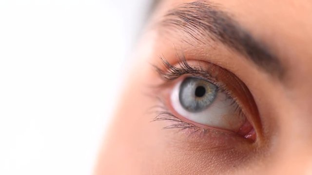 Beautiful female blue eye closeup. Young woman eye blinking and looking up, over white background. 4K UHD video 3840X2160