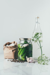 glass jar with preserved cucumbers, glass bottle with dill and salt on table