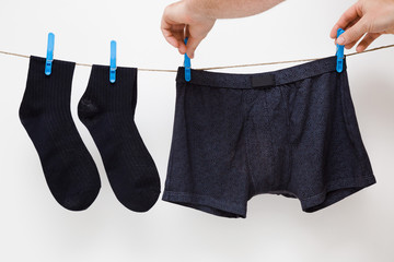 Man's hands hanging clean black socks and boxer shorts. Underwear drying on laundry rope at white...