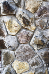 An ancient wall of stones of various geometric shapes of grey, yellow and brown colors als texture