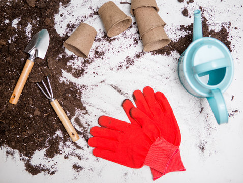 Photo of top soil for transplanting plants, rake, scoop, watering can, red gloves