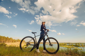 Fototapeta na wymiar The beautiful girl is standing by bicycle. Senior woman riding a bike beside a lake. A female biker take a rest after biking
