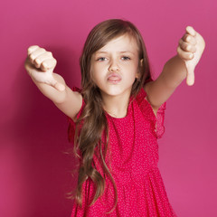 Little 8 years old girl make some emotional gesture with her hands on a pink neutral background. She has long brunette hair and wear red summer dress. Funny expression on her face