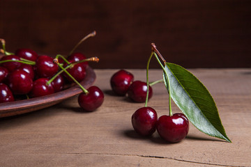 Clay plate with red sweet cherry on wooden background.