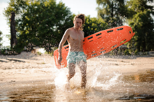 Sexy Long-haired Beach Lifeguard Running In Water With Life-saving Equipment