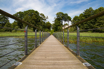 Fototapeta premium Holzbrücke über wasser mit leicht bewöltem Himmel und Bäumen