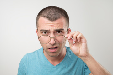 Fototapeta premium Wow facial emotion concept. Surprised young man with opened mouth touching glasses.