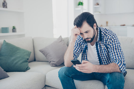 Portrait of tired alone serious man sitting indoor using smart phone, internet, checking email, having problem in relationship chatting with his girlfriend worry about bad news