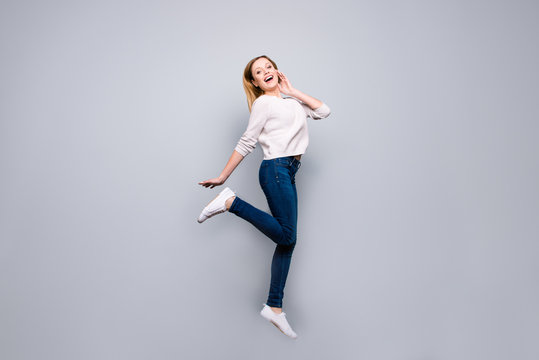 Portrait of trendy charming pretty funny comic blonde girl jumping in the air with raised leg posing looking at camera isolated on grey background, sport concept
