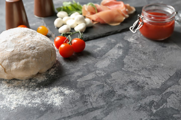 Raw dough and ingredients for pizza on grey textured background