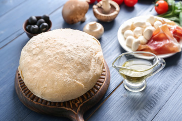 Raw dough with ingredients for pizza on color wooden background