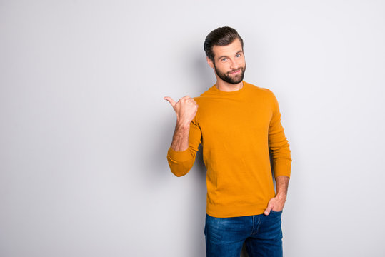 Portrait of cheerful attractive joyful confident guy keeping hand in pocket of jeans hinting pointing on copyspace behind his back isolated on gray background