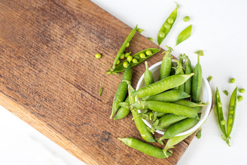 A pods of peas on wooden board on white. Copy space
