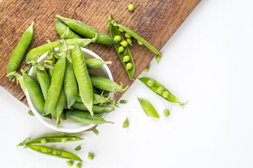 A pods of peas on wooden board on white. Copy space