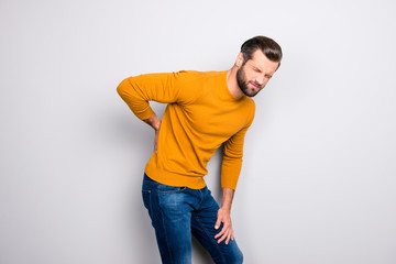 Side profile half-turned portrait of grimacing sad upset unhappy with serious pain in back man wearing yellow tight sweater and jeans isolated on gray background copy-space