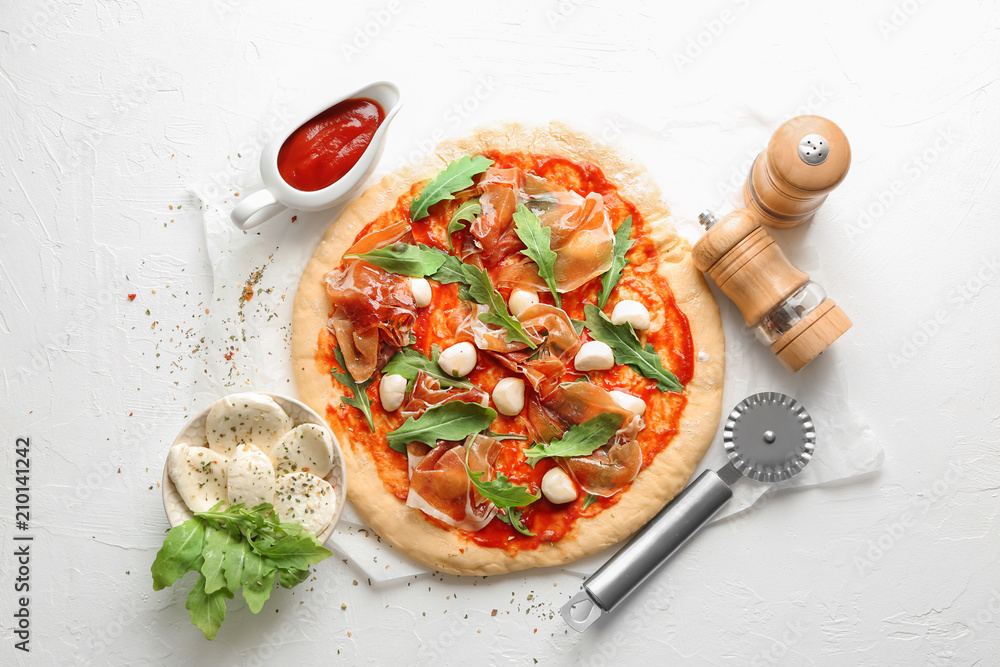 Wall mural Raw pizza with tomato sauce and ingredients on light background