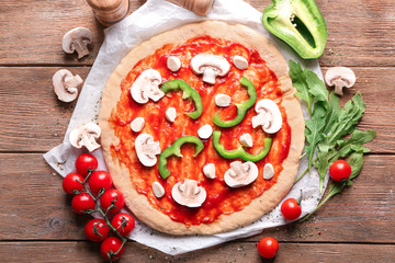 Raw pizza with tomato sauce and ingredients on table