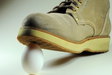White egg under the sole of a boot. Concept of risky situation.