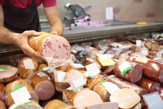 Male seller holding piece of deli meat in butcher shop