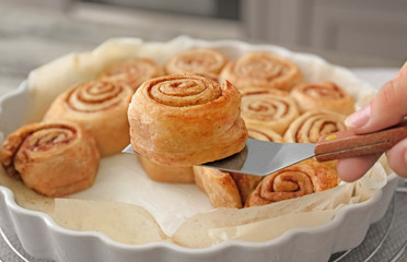 Woman taking tasty cinnamon bun from baking dish, closeup