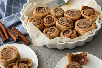 Baking dish and plates with tasty cinnamon buns on table