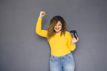 Cute brunette plus size woman with curly hair in yellow sweater and jeans standing on a neutral...
