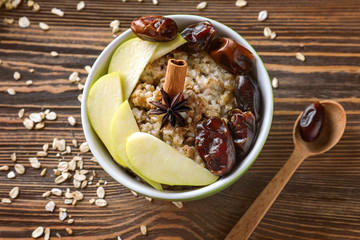 Bowl with tasty oatmeal, fruits and spices on wooden background