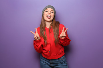 Attractive hipster girl showing victory gesture on color background
