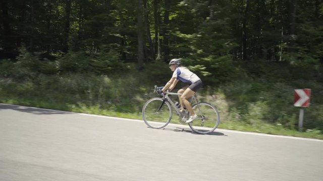 4k sport footage, woman on racing bicycle cycling uphill on asphalt street in forest
