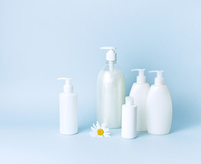 Cosmetic bottle containers with chamomile flowers on a blue minimalistic background flat lay. Blank label for branding mock-up. Natural beauty product concept.