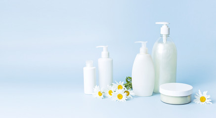 Cosmetic bottle containers with chamomile flowers on a blue minimalistic background flat lay. Blank label for branding mock-up. Natural beauty product concept.
