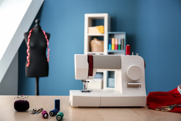 Sewing machine with accessories on table in tailor's workshop