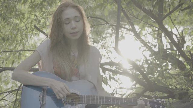 Red-haired girl playing in a park on a guitar, color profile Slog3