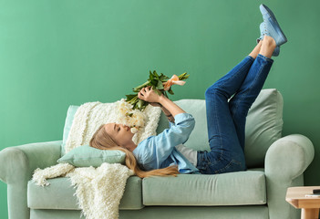 Attractive young woman with beautiful flowers lying on sofa at home
