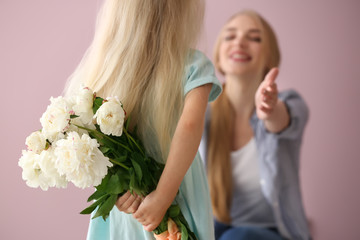 Cute little girl hiding bouquet of flowers for mother behind her back on color background