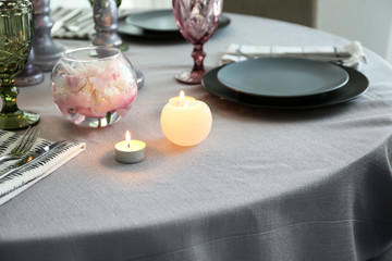 Burning candles with dishware on table in dining room
