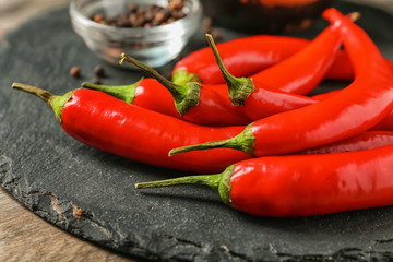Slate plate with fresh chili peppers on wooden background, closeup