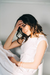 Portrait  of beautiful brunette sitting in a white dress. Vertical orientation.