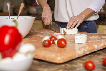 Beautiful young brunette woman in casual outfit cooking in the kitchen in her home. Luxury rich interior