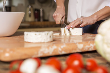 Beautiful young brunette woman in casual outfit cooking in the kitchen in her home. Luxury rich interior