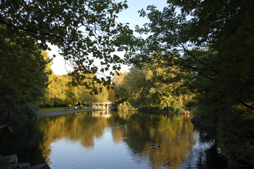 Fototapeta na wymiar pond in an autumn park, calm water and lush vegetation, small figures of relaxing people, Ireland