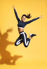 Sporty smiling woman jumping up in silhouette on yellow background. Dynamic movement. Sport and healthy lifestyle