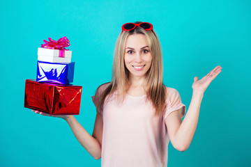 cheerful attractive surprised and shocked woman smiling and holding a lot of box with a gift on a blue background in the studio.