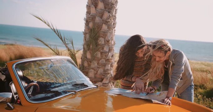 Women with retro convertible car reading map on island holidays