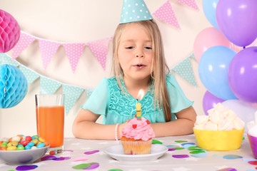 Little girl blowing out candle on birthday cupcake at home - Powered by Adobe