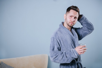 Portrait of handsome young man holding glass of cognac.Portrait of a handsome bearded Businessman in grey bathrobe drinking a Whiskey