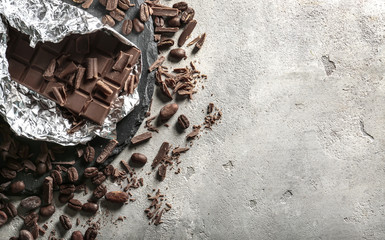 Tasty milk chocolate bar and chunks with coffee beans on table