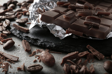 Tasty milk chocolate bar and chunks with coffee beans on table, closeup